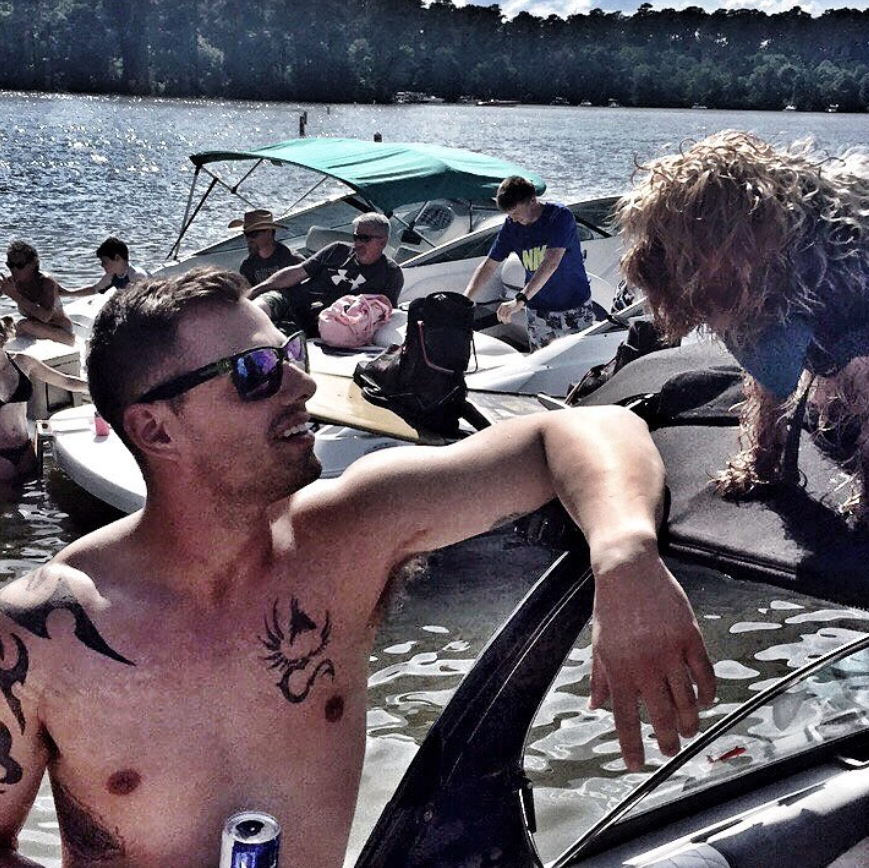 Alex relaxing on a boat with his dog Zeus, surrounded by other boats and people enjoying a sunny day on a lake in Houston, TX.