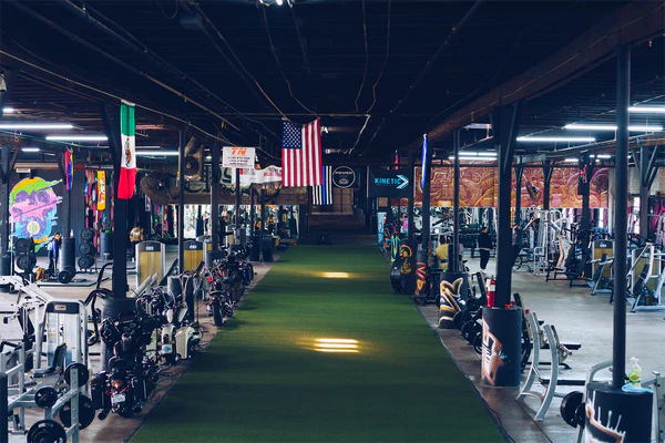 The interior of Believe HTX gym in Houston, TX, featuring a turf training area, weightlifting equipment, and international flags, showcasing a top-tier fitness facility for athletes and professionals.